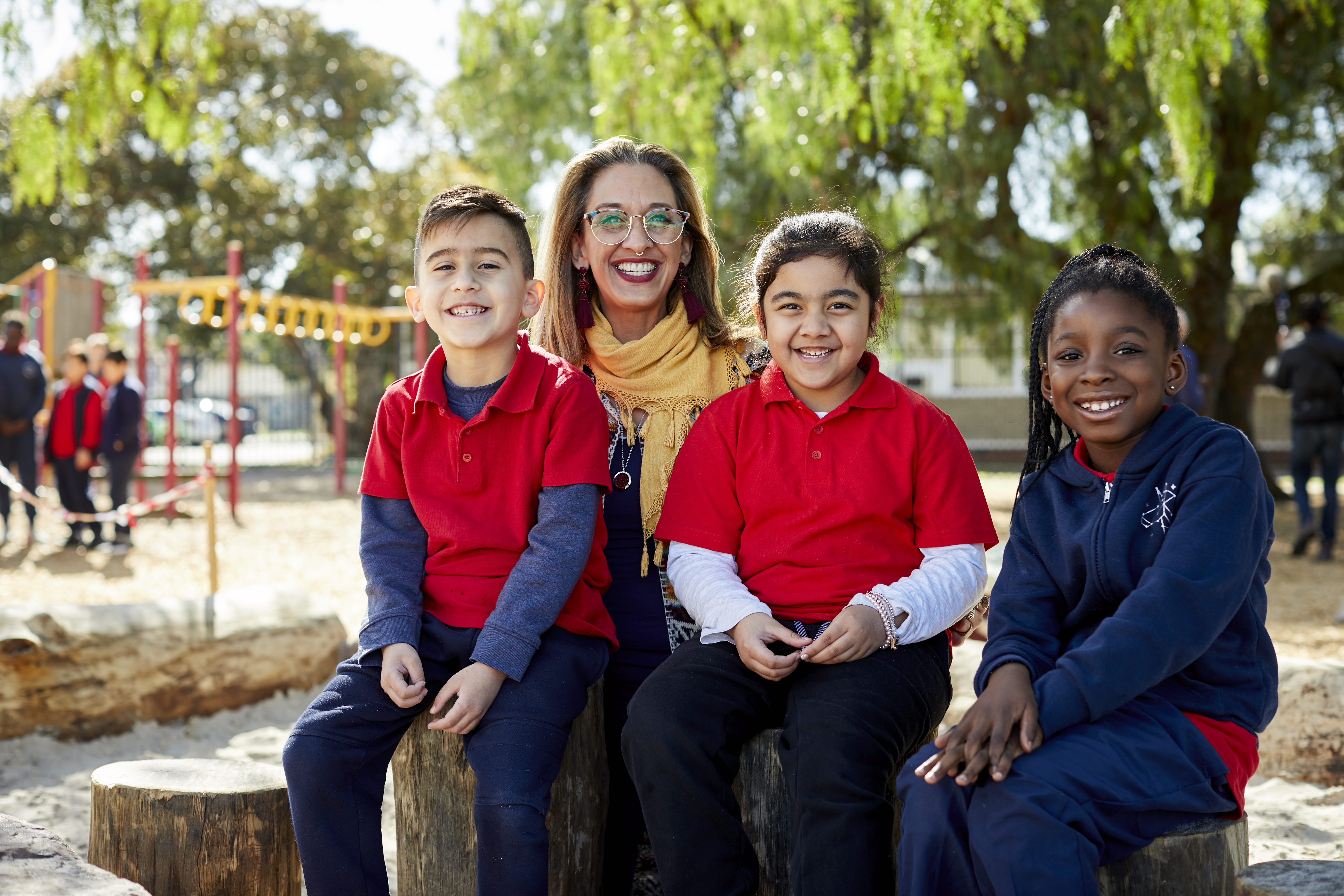 An educator with three primary school students sitting in a playground and smiling.