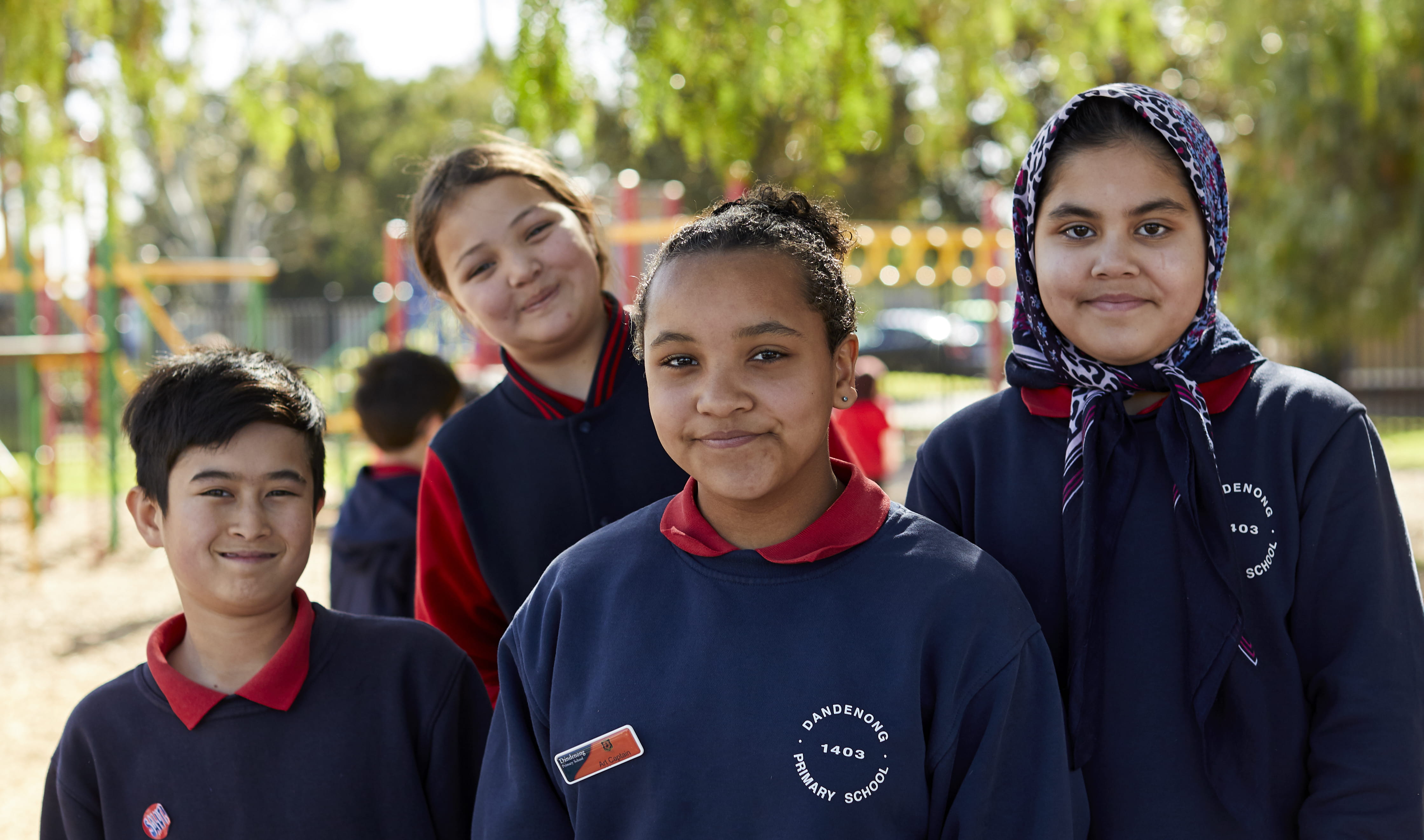 Four primary school age children standing in a playground and smiling to the camera.