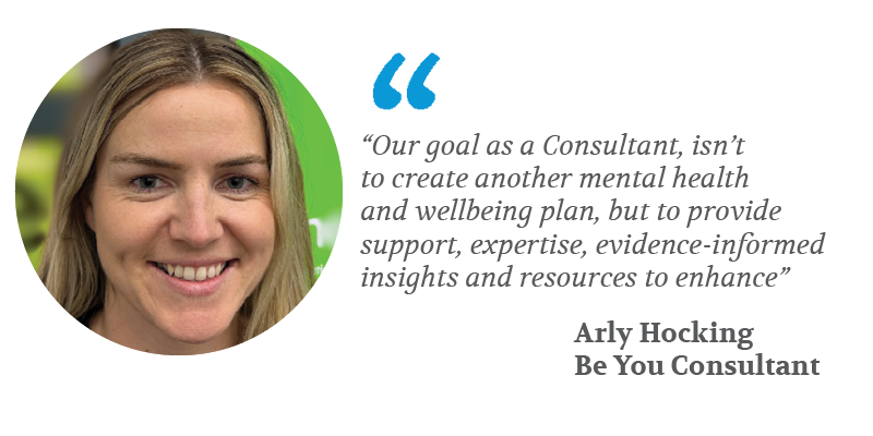 The image features a photo of a woman with blonde hair smiling, alongside a quote. The quote reads: "Our goal as a Consultant, isn’t to create another mental health and wellbeing plan, but to provide support, expertise, evidence-informed insights and resources to enhance" – Arly Hocking, Be You Consultant.  The quote is accompanied by stylised quotation marks and the consultant's name and role are in bold text. The background behind the woman is blurred.