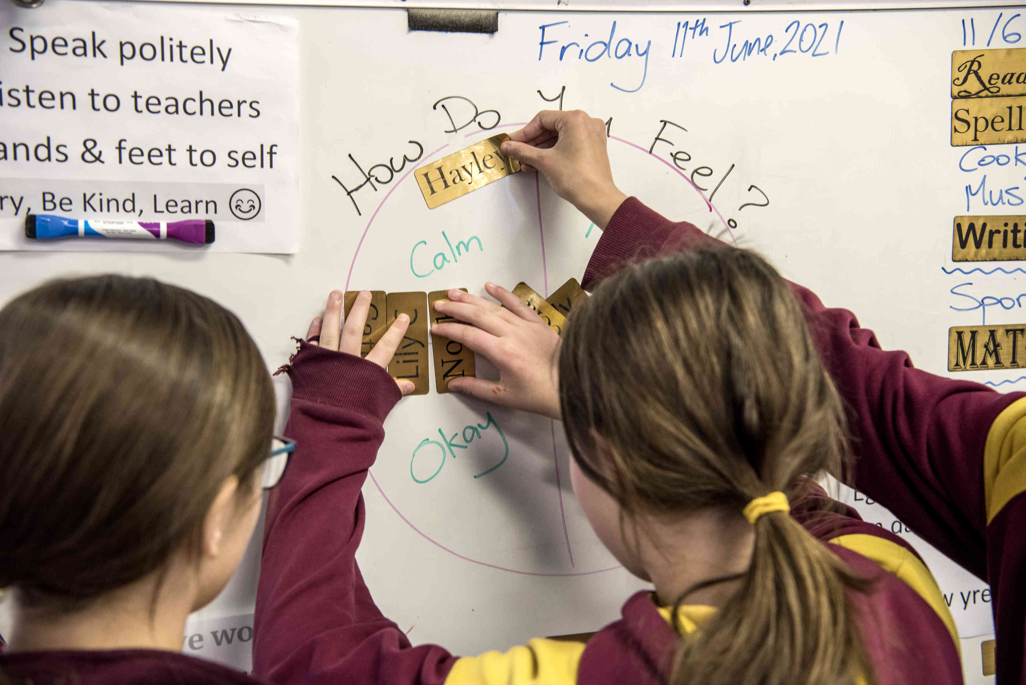 Children in a classroom, using a 'How do you feel?' chart