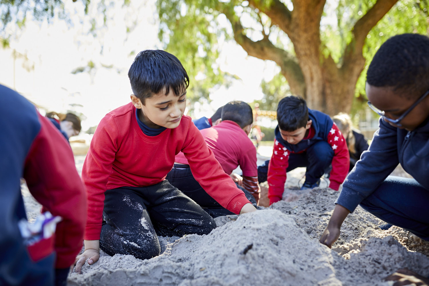 A group of multi ethnic primary school aged students playing in a sandpit.