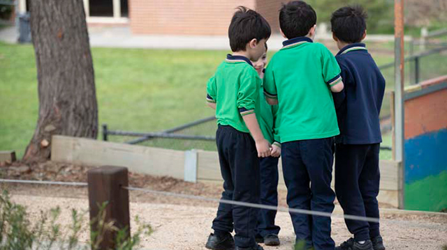 A group of three primary school aged students huddled together with their backs to the camera.