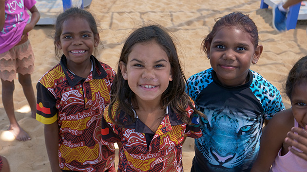 Three young Aboriginal and Torres Strait Islander girls looking up and smiling at the camera.