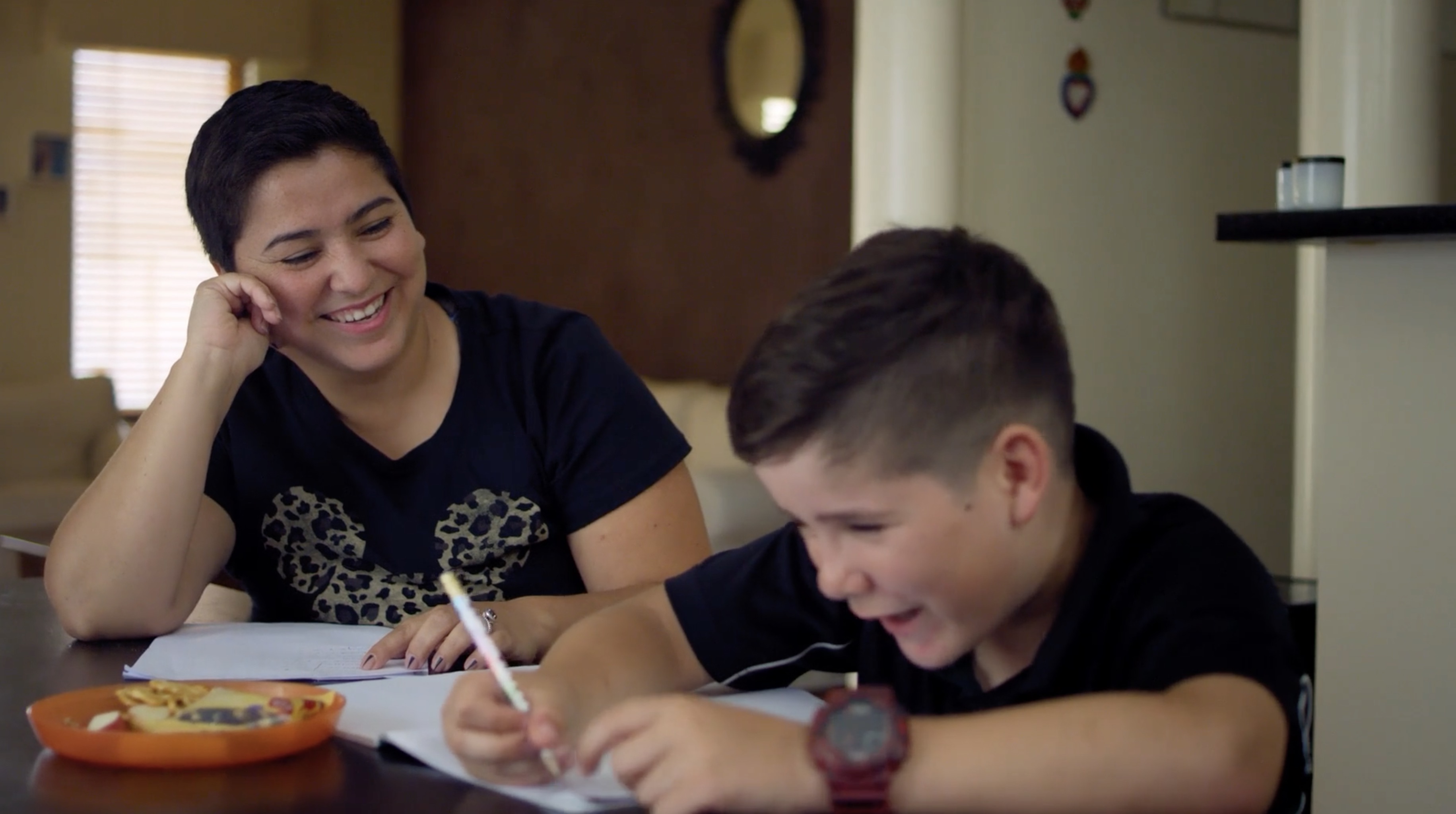 A child writing with an educator looking on, smiling 