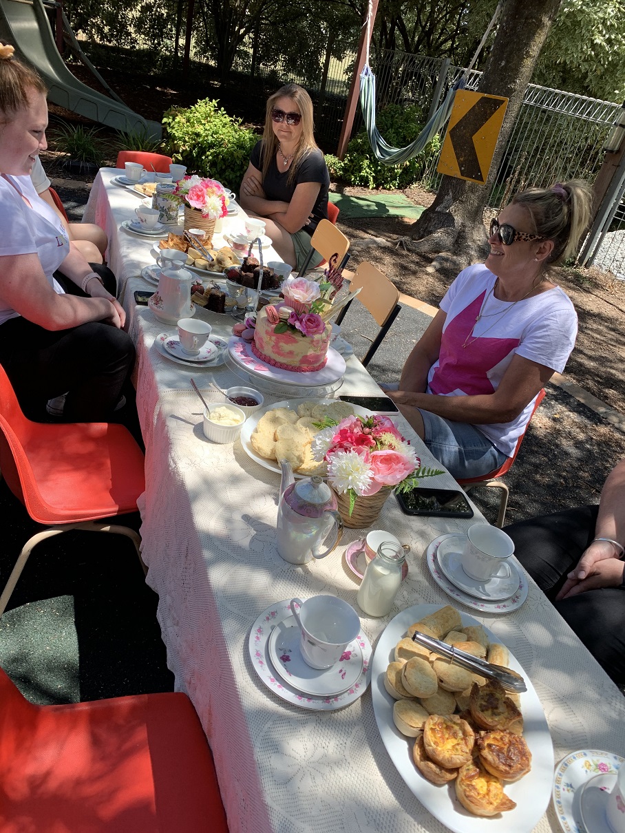 A group of adults, sitting around an outdoor table enjoying high tea
