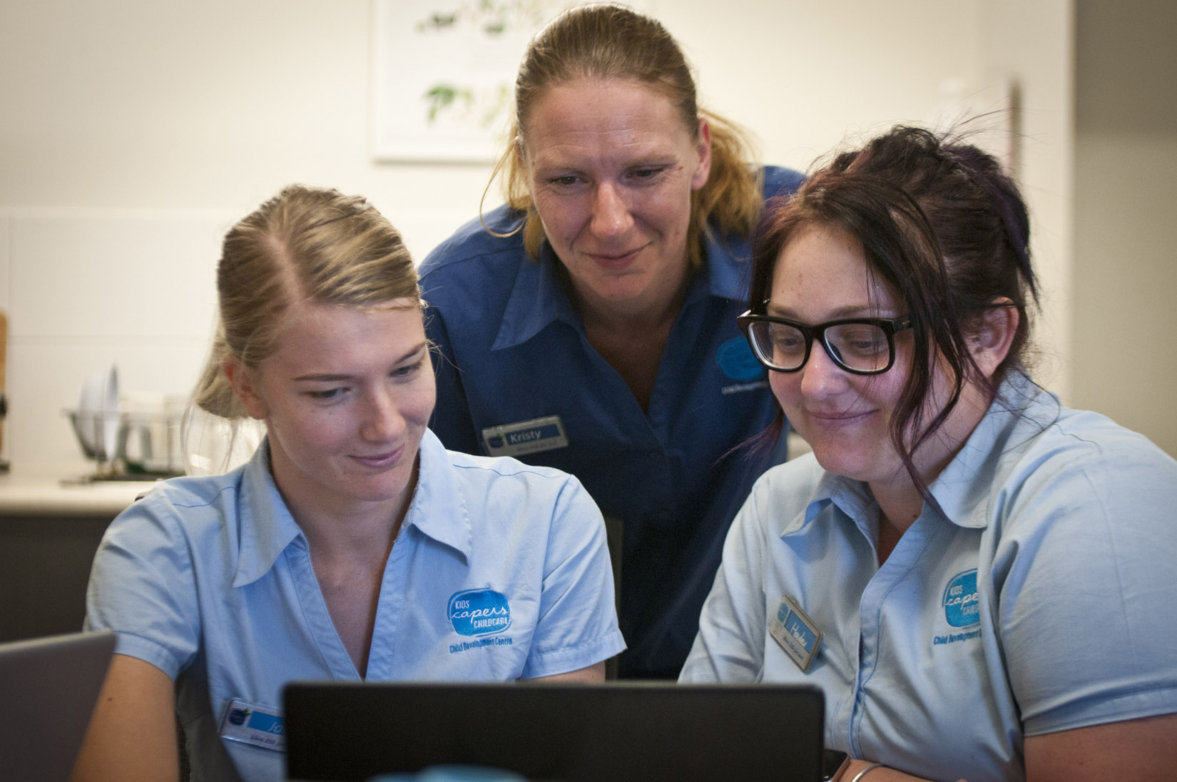 Two students working at a computer, with an educator looking on 