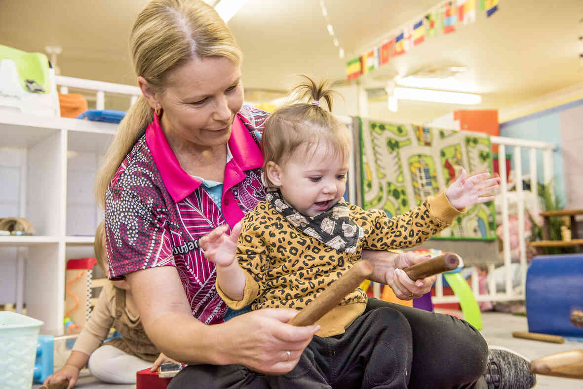 An adult with a baby, playing with clapping sticks