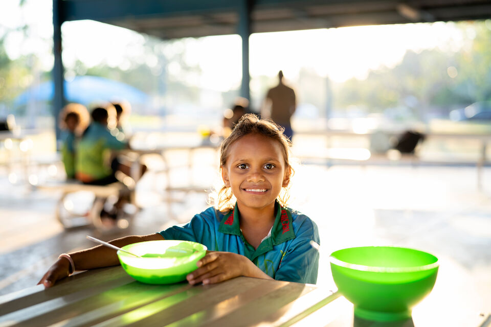 A young child with a bowl of food, smiling at the camera