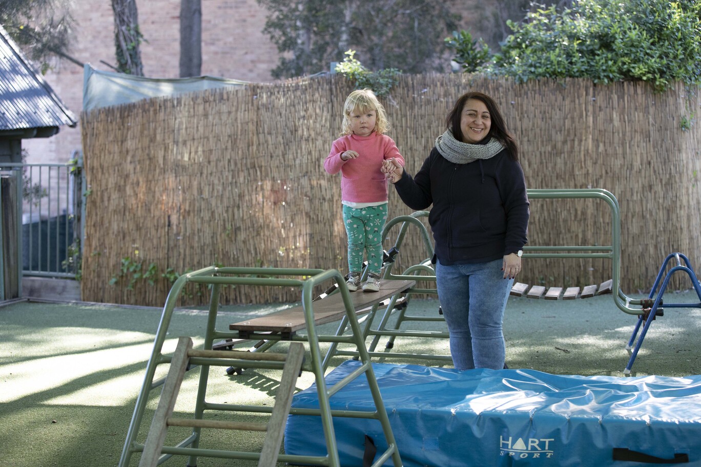 An adult holding the hand of a young child walking along a balance beam