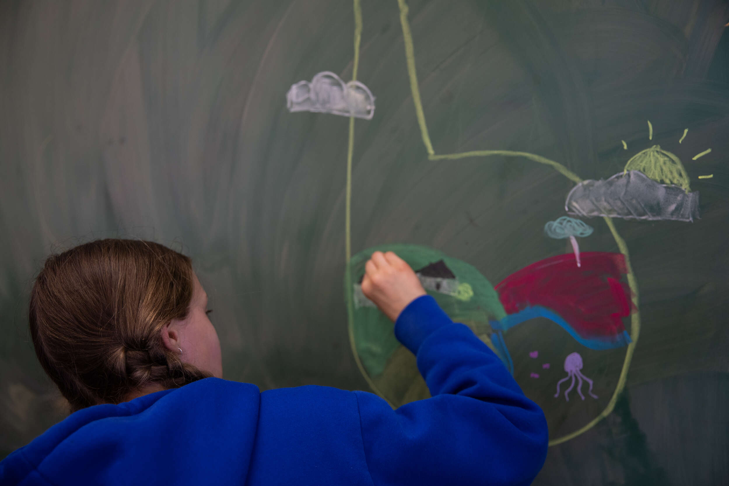 A young person drawing the Be You logo on a blackboard