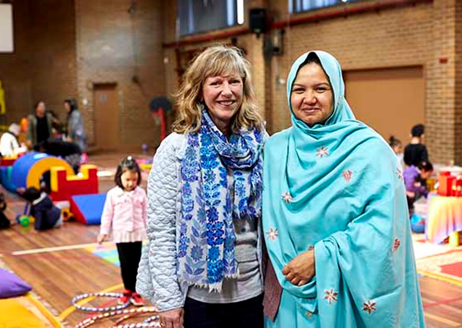 Two adults in a school hall, smiling at the camera