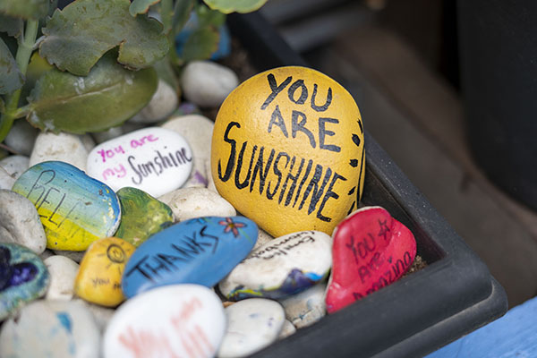 A pile of stones that have been painted with positive messages, including a bright yellow stone that has the message you are sunshine
