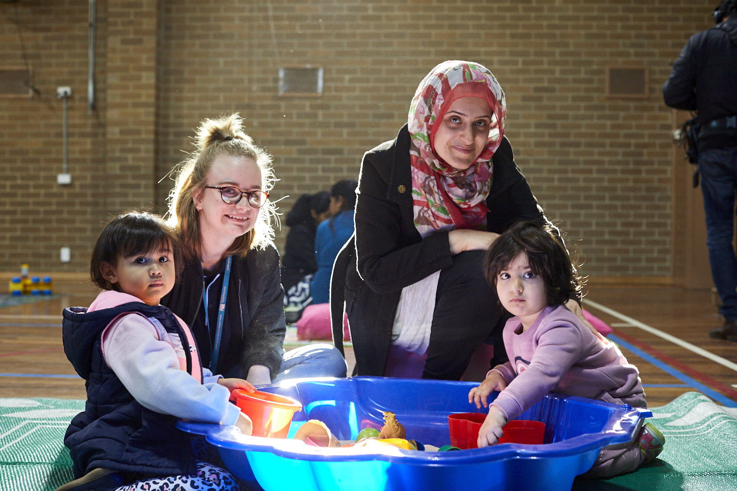 Two adults with two young children playing with toys in a sandpit