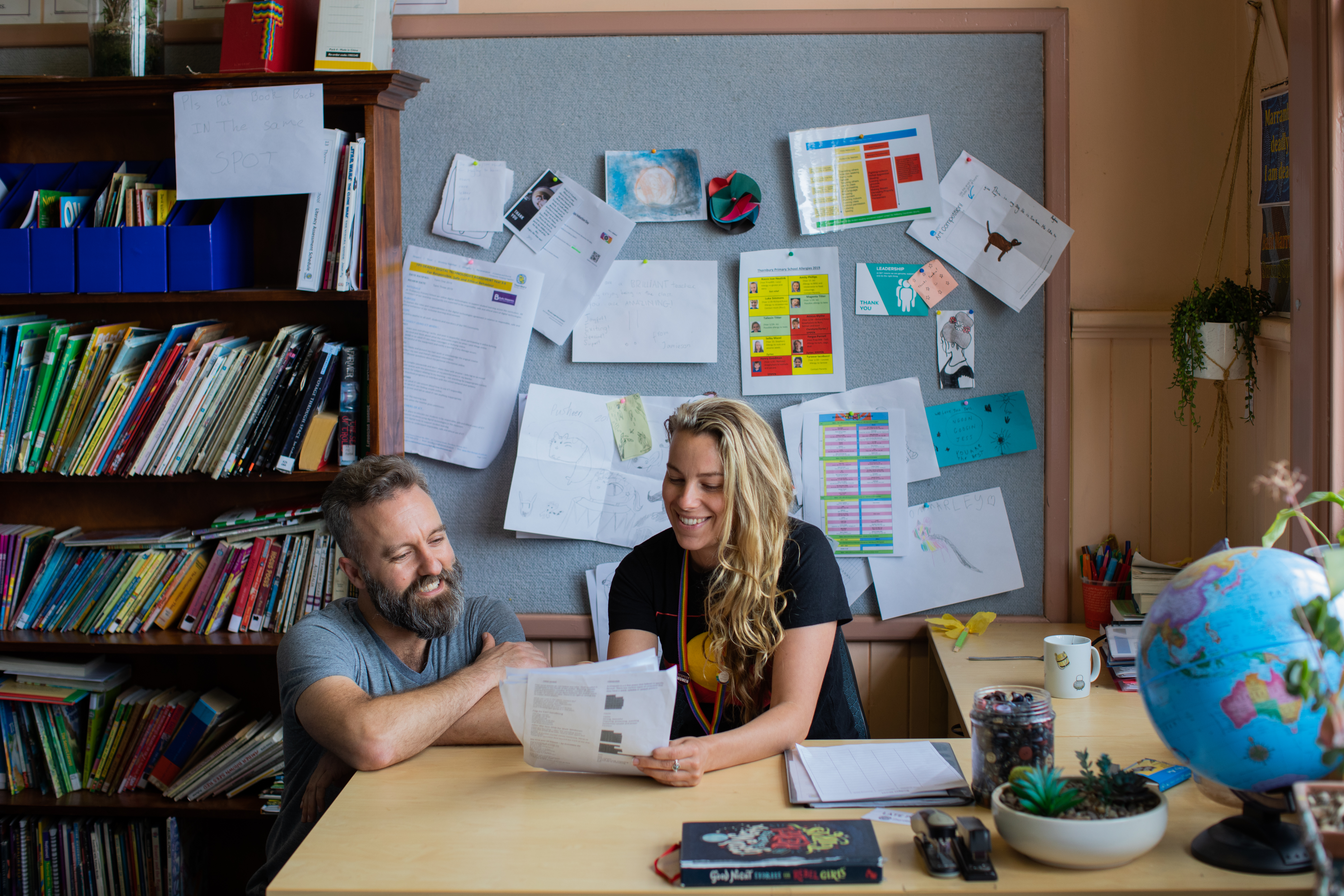 Two educators at a desk in a classroom looking at some pieces of paper together.