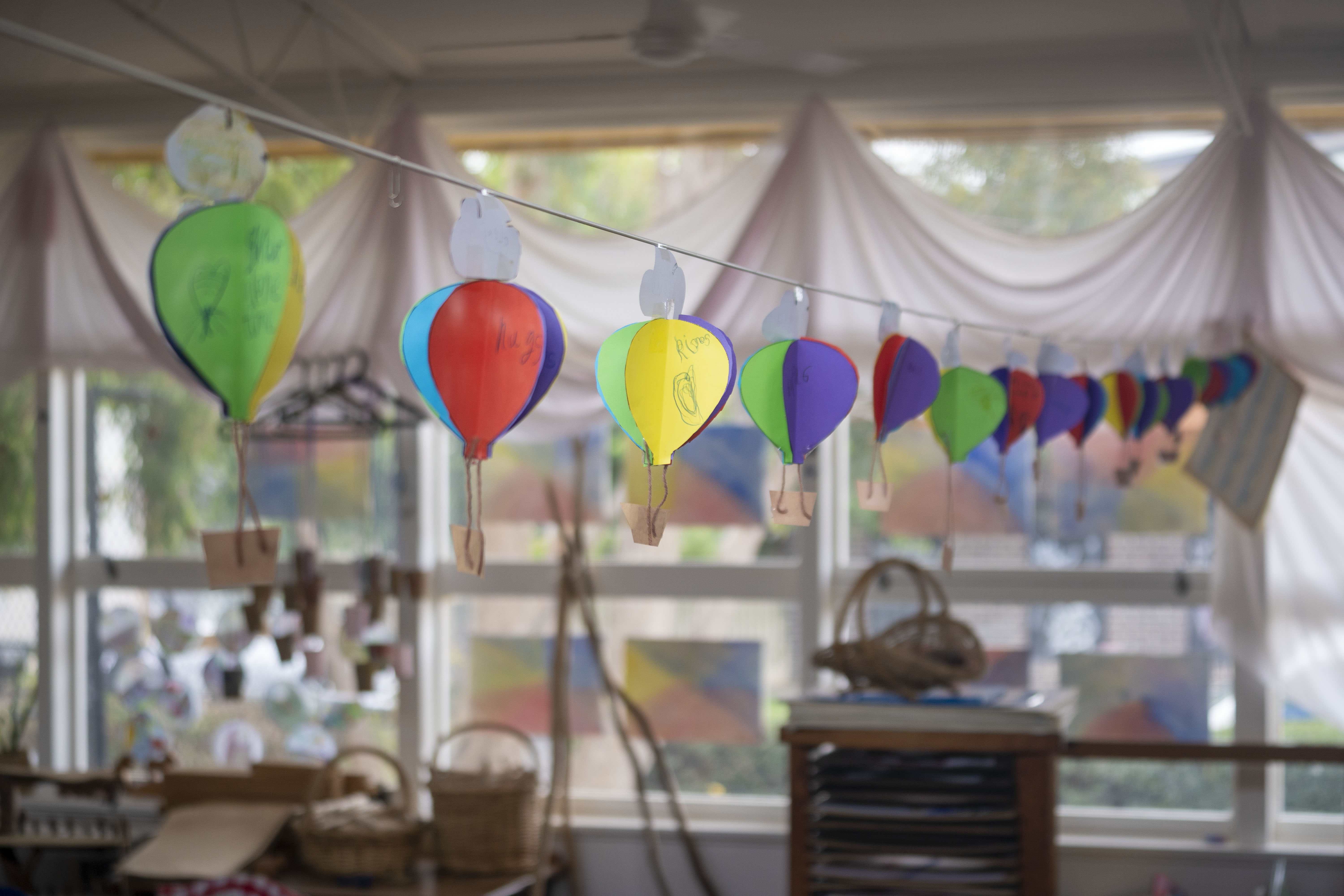 A string of colourful paper hot air balloons hanging up in a primary school classroom. 