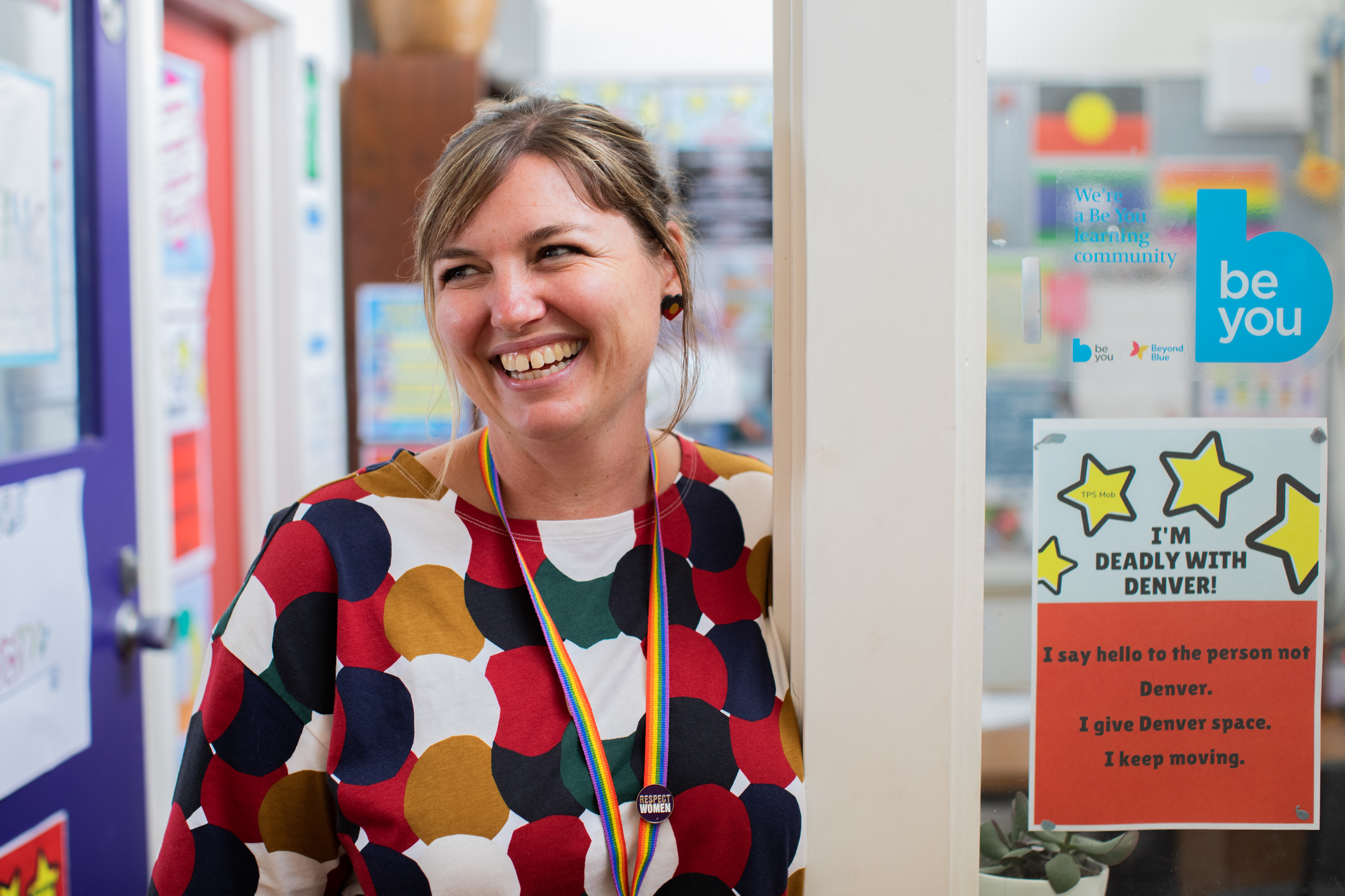An educator standing in the doorway to an office, looking to their right and smiling.