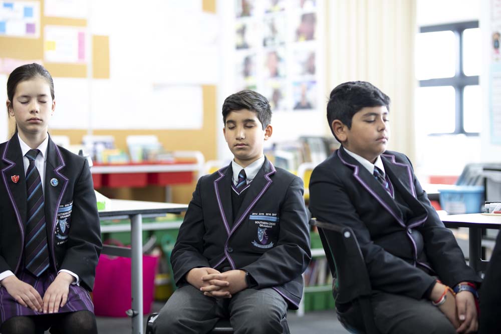Young people in a classroom, practising mindfulness with their eyes closed 