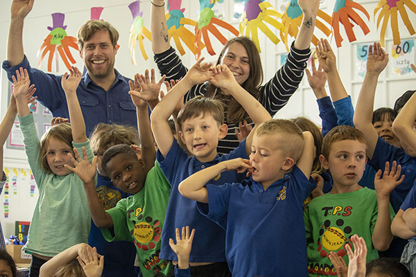 Two educators and a group of children, with their arms in the air