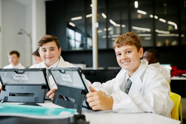 Two young people working on laptops, smiling at the camera