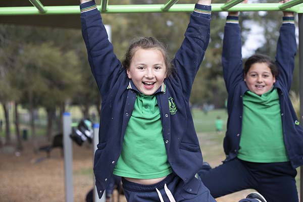 Two children hanging from monkey bars, smiling at the camera