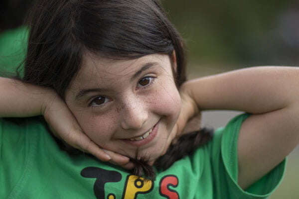 A young child with hands around her face, smiling at the camera