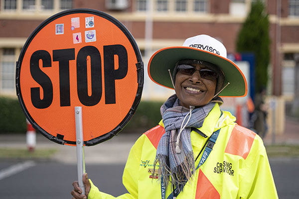 A crossing supervisor holding a stop sign, smiling at the camera