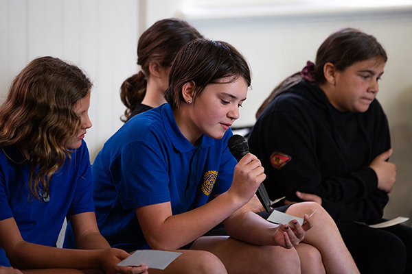 A group of young people sitting in a classroom, with one student holding a microphone
