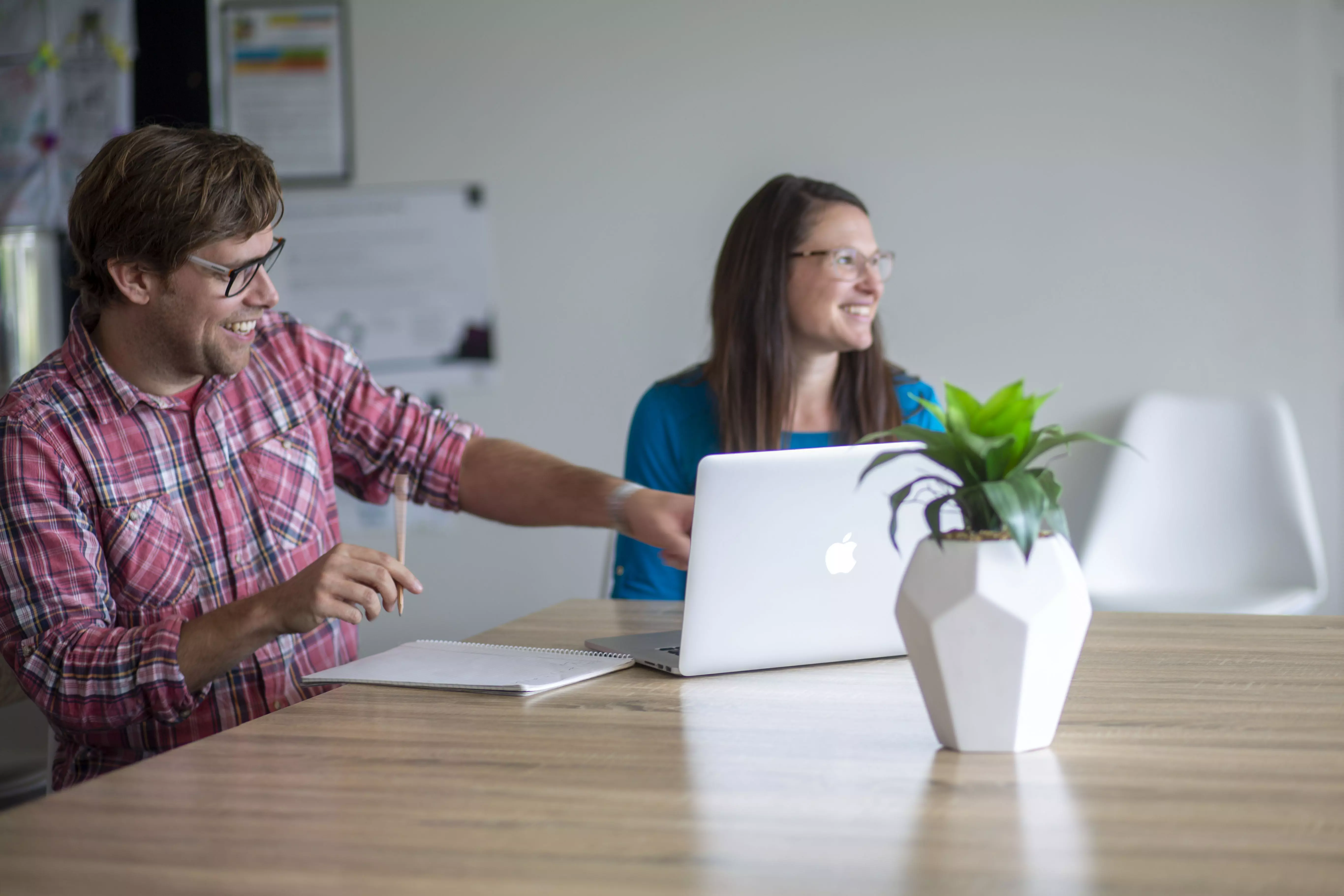 Two adults sitting at a table, smiling and pointing at a laptop