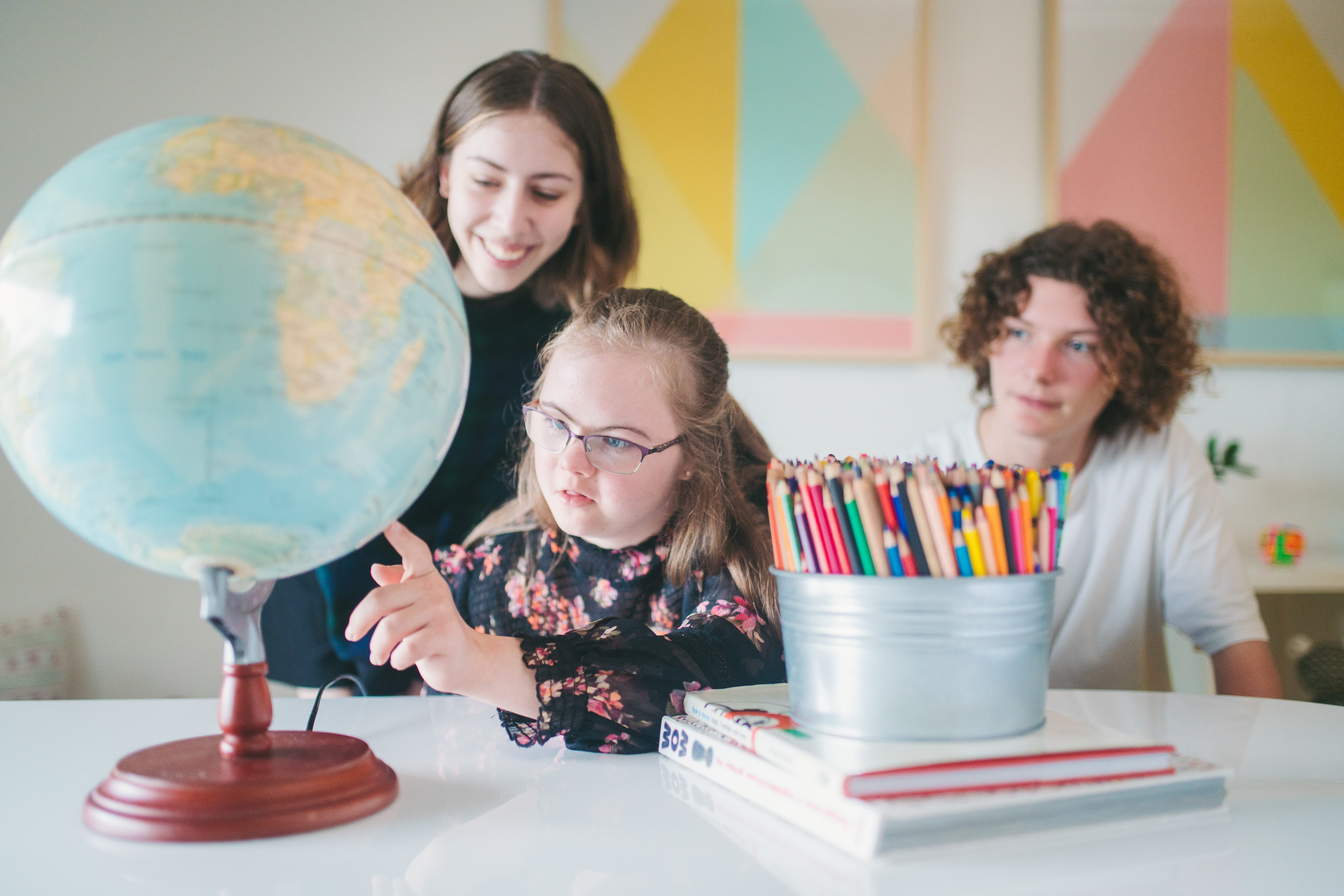 A young child spinning a globe of the world with two adults looking on